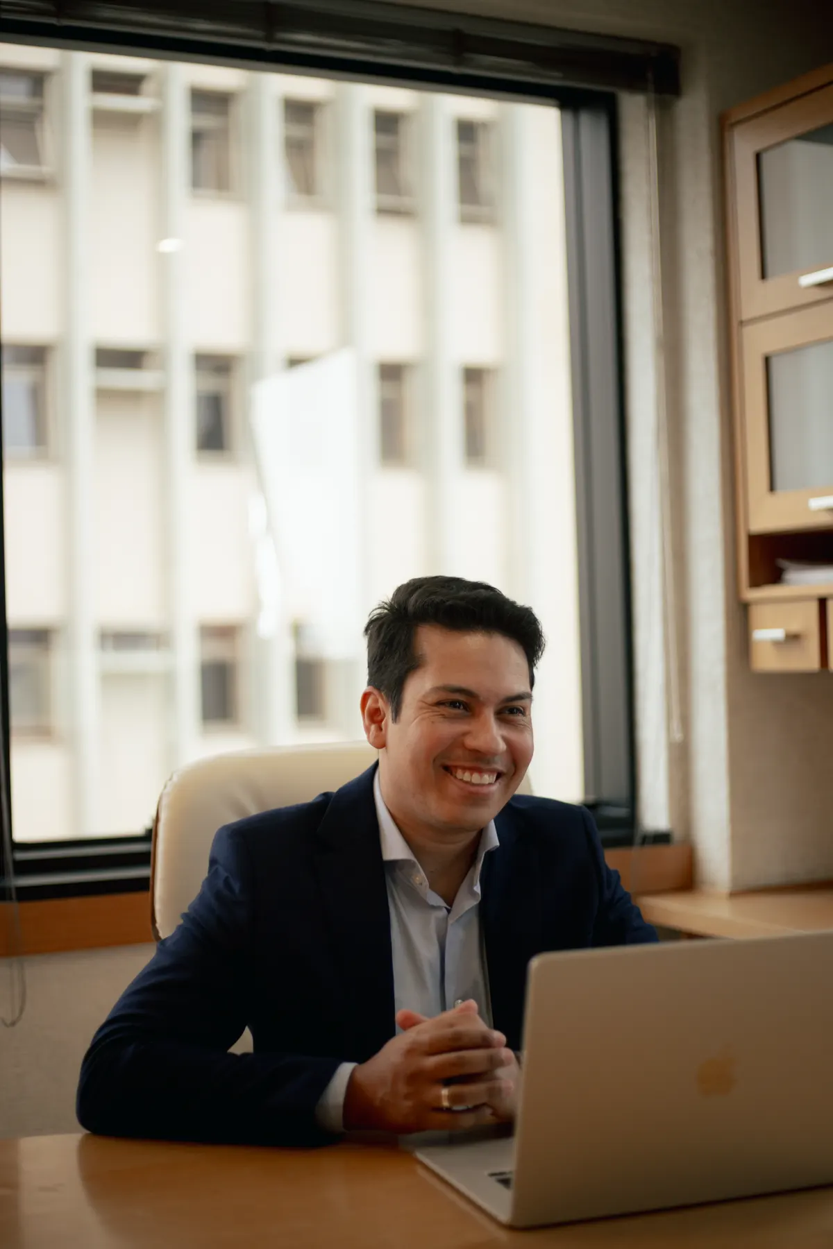 Felipe Borges sorrindo, sentado à mesa do escritório